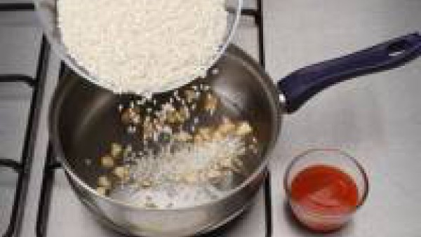 Pon el aceite a calentar. Después, incorpora los ajos pelados y cortados a trocitos pequeños. Cuando empiecen a tomar color, añade el arroz y la salsa de Tomate Frito Gallina Blanca.