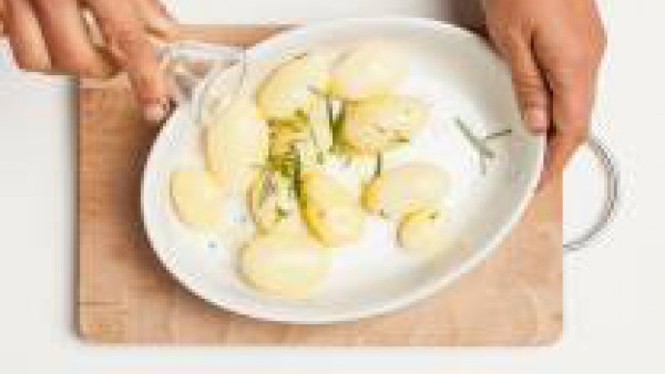 Precalienta el horno a 200°C. Pela las patatas y colócalas en una fuente untada con 1 cucharada de aceite de oliva virgen extra. Espolvorea con sal, romero y tomillo picado. Hornéalo solo cuando el ho