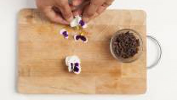 Cuando la panacota esté lista sírvela en los platos con la ayuda del papel en la que está envuelta. Decora con el chocolate y los pétalos.